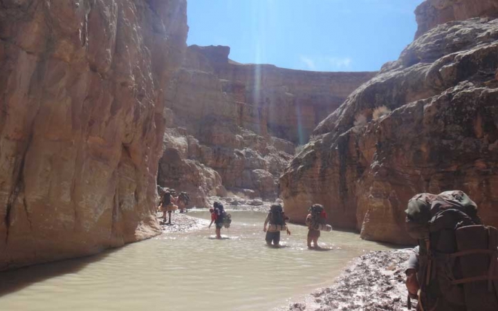 A group of students cross a canyon filled with ankle-deep water